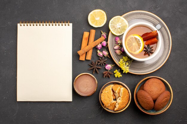 Vista superior de la taza de té con galletas y rodajas de limón en la superficie oscura té azúcar fruta galleta galletas dulces