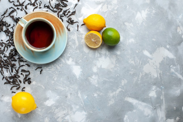 Vista superior de la taza de té con granos de té secos frescos y limón en la mesa de luz, desayuno de bebida de té