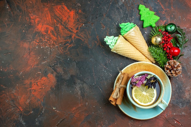 Vista superior de la taza de té helados palitos de canela rama de un árbol de Navidad con juguetes en el espacio libre de la mesa de color rojo oscuro