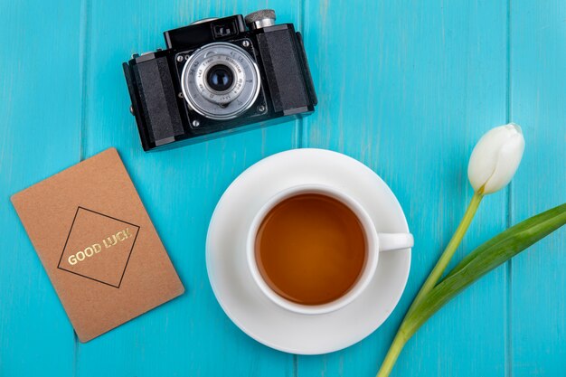 Vista superior de una taza de té con hermoso tulipán blanco con cámara sobre un fondo de madera azul