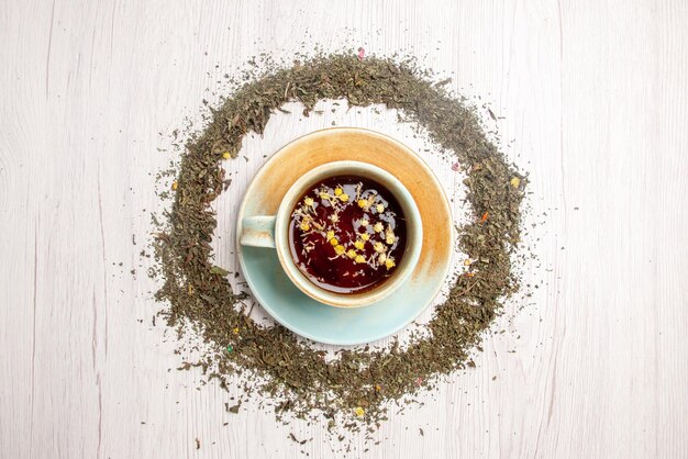 Vista superior de la taza de té de hierbas de té de hierbas y hierbas a su alrededor en la mesa blanca