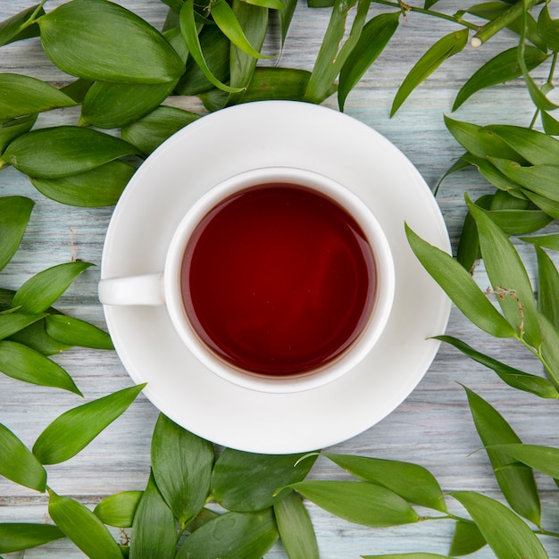 Vista superior de una taza de té con hojas verdes en madera gris