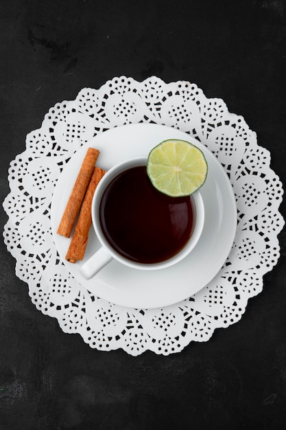 Foto gratuita vista superior de la taza de té con limón y canela en bolsa de té sobre tapete de papel sobre superficie negra