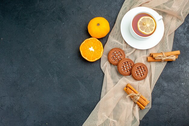 Vista superior de una taza de té con limón canela palitos de galletas en un mantón beige naranja en el espacio libre de superficie oscura