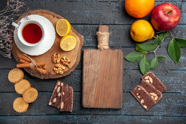 Vista superior de una taza de té con limón y dulces en la mesa oscura