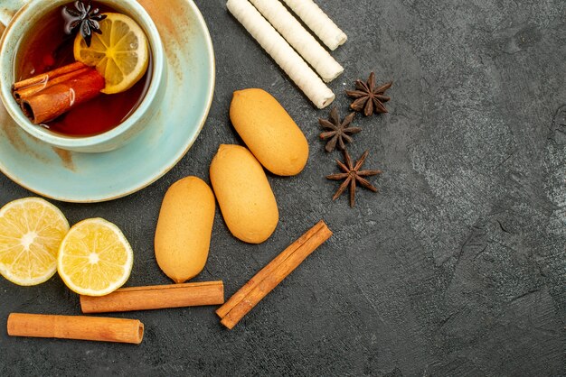 Vista superior de una taza de té con limón y galletas en el fondo oscuro