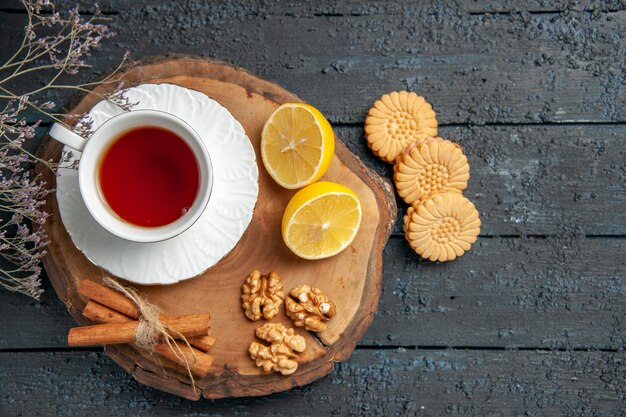 Vista superior de una taza de té con limón y galletas en la mesa oscura