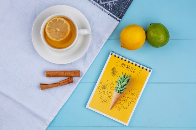 Vista superior de la taza de té con limón y lima canela sobre una toalla blanca con un cuaderno sobre una superficie azul