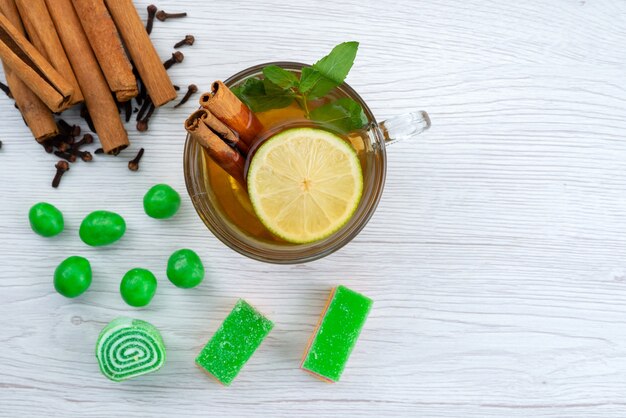 Vista superior de una taza de té con limón, menta y canela en blanco, dulces de postre de té