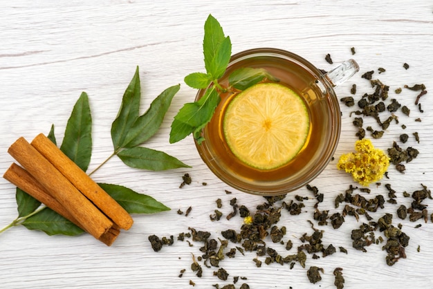 Vista superior de una taza de té con limón, menta y canela en blanco, dulces de postre de té