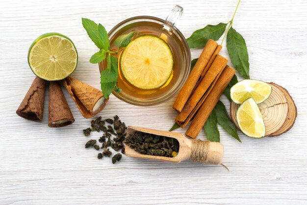 Vista superior de una taza de té con limón, menta y canela en blanco, dulces de postre de té