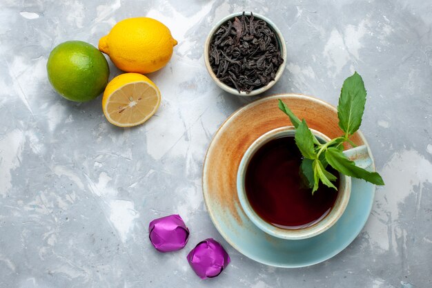 Vista superior de la taza de té con limones frescos caramelos y té seco en la mesa de luz, color cítrico de frutas de té