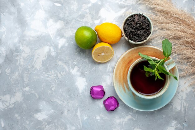 Vista superior de la taza de té con limones frescos caramelos y té seco en la mesa de luz, té de frutas cítricas