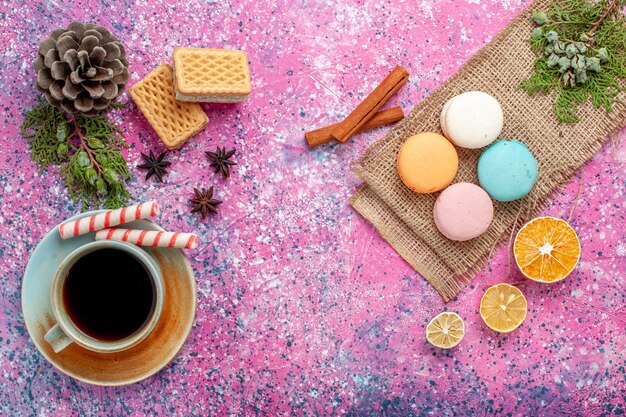 Vista superior de la taza de té con macarons franceses en el escritorio rosa