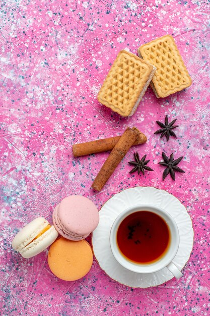 Vista superior de la taza de té con macarons franceses y galletas en el escritorio rosa claro