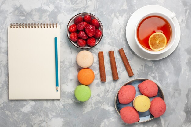 Vista superior de una taza de té con macarons franceses y pasteles en una superficie blanca clara