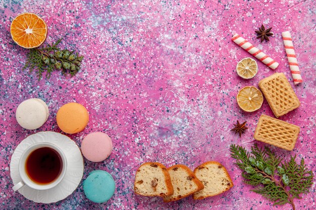 Vista superior de la taza de té con macarons franceses y waffles en superficie rosa