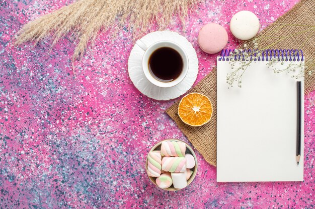 Vista superior de la taza de té con macarons en superficie rosa