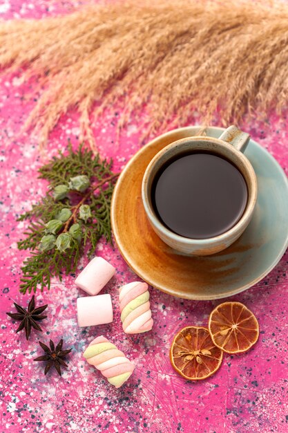 Vista superior de una taza de té con malvaviscos en el escritorio de color rosa claro.