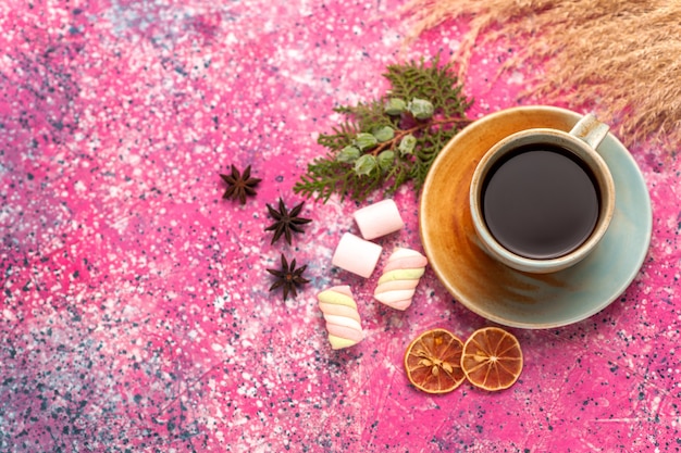 Vista superior de una taza de té con malvaviscos en el escritorio de color rosa claro.