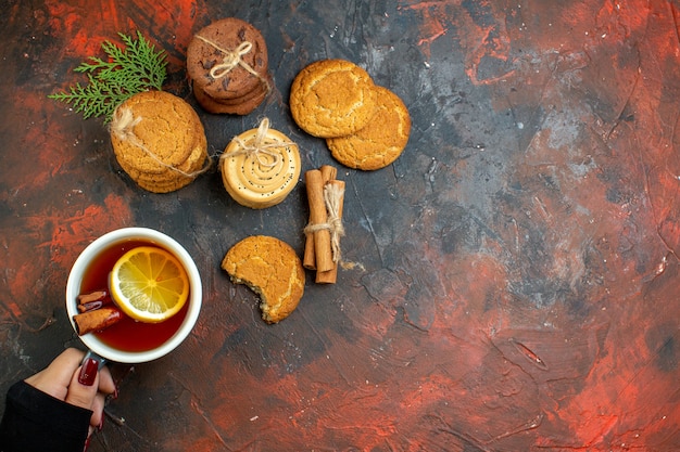 Vista superior de la taza de té en la mano femenina canela palitos de galletas atadas con una cuerda en el espacio libre de la mesa de color rojo oscuro