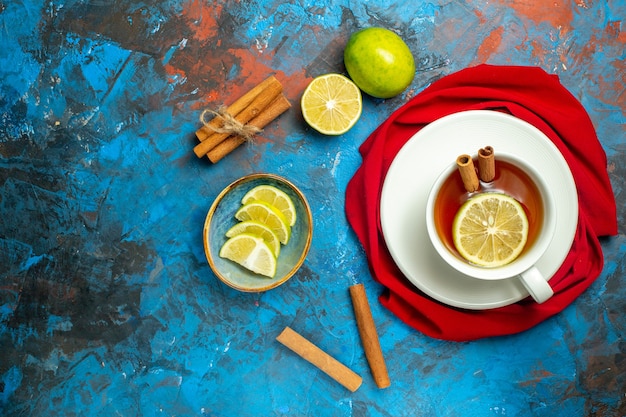 Vista superior de una taza de té con un mantón rojo de limón y canela en el lugar de la copia de la superficie roja azul
