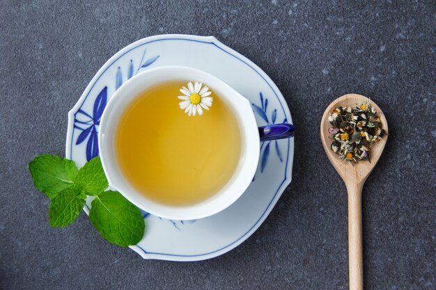 Vista superior de una taza de té de manzanilla con hojas de menta y hierbas de manzanilla en una cuchara.