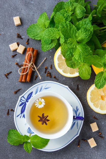 Vista superior de una taza de té de manzanilla con hojas de menta, limón, azúcar, canela seca.