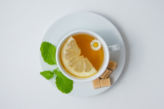 Vista superior de una taza de té de manzanilla con limón, hojas de menta, azúcar en la superficie blanca. horizontal