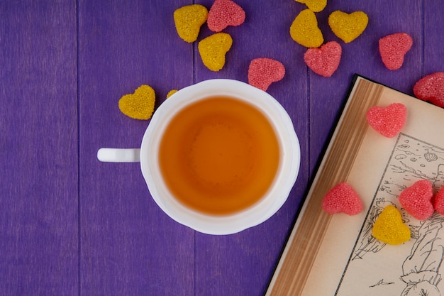 Foto gratuita vista superior de la taza de té con mermeladas y libro abierto sobre fondo morado