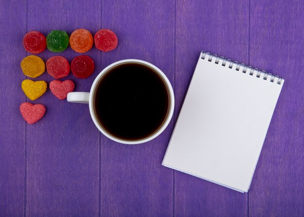 Vista superior de la taza de té con mermeladas y notas sobre fondo morado