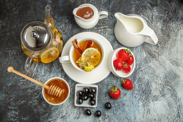 Vista superior de la taza de té con miel, aceitunas y frutas en la superficie oscura, comida de desayuno por la mañana