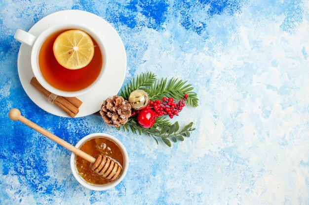 Vista superior de la taza de té de miel y palo de miel en un tazón de fuente de la rama de un árbol de Navidad en el espacio libre de la mesa azul