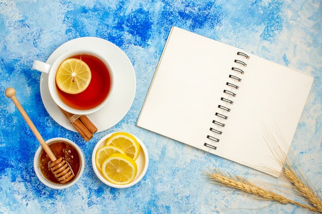 Vista superior de la taza de té de miel en un tazón de fuente de rodajas de limón portátil en la mesa azul