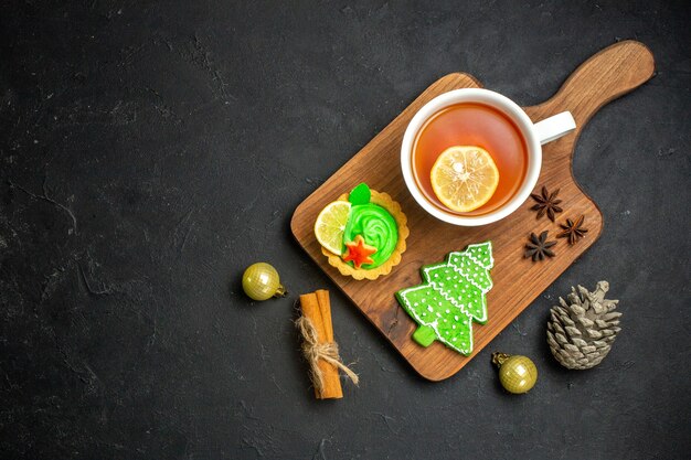 Vista superior de una taza de té negro accesorios de año nuevo cono de coníferas y limas de canela sobre fondo negro