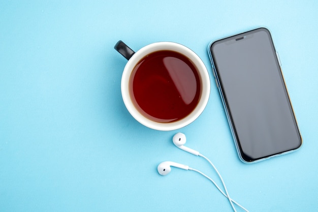 Vista superior de una taza de té negro para auriculares de teléfono móvil sobre fondo azul.