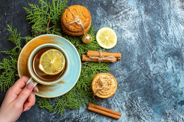 Vista superior de una taza de té negro en ramas de abeto y galletas apiladas canela limones limón sobre fondo oscuro