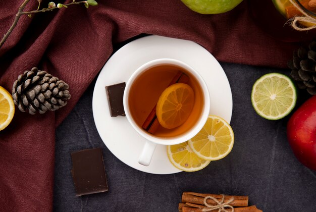 Vista superior de una taza de té negro con una rodaja de limón, canela, chocolate negro, manzanas, cono de abeto y rodaja de limón