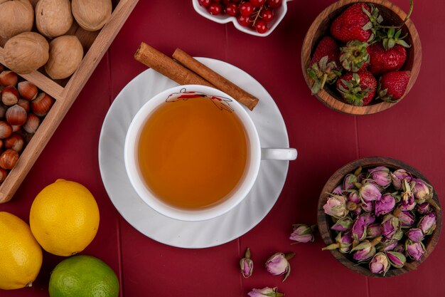 Vista superior taza de té con nueces con avellanas cacahuetes grosellas rojas y fresas sobre un fondo rojo.