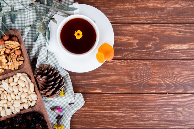 Vista superior de una taza de té con nueces mixtas y frutas secas en madera con espacio de copia