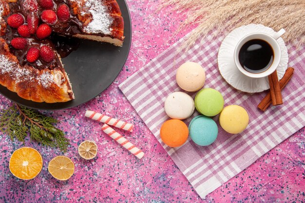 Vista superior de la taza de té con pastel de canela y macarons franceses en el escritorio rosa pastel galleta galleta azúcar dulce