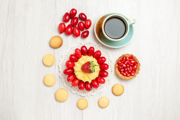 Vista superior de la taza de té con pastel cremoso y frutas en el escritorio blanco