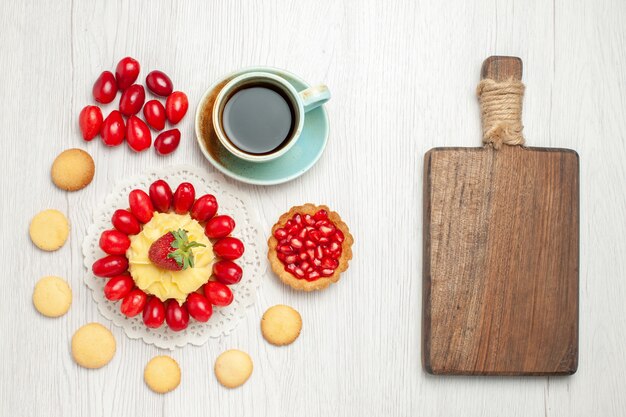 Vista superior de una taza de té con pastel cremoso y frutas en el piso blanco