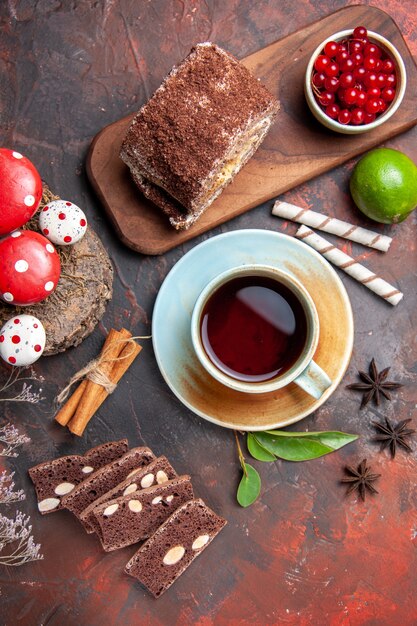 Vista superior de la taza de té con pastel y rollo de galletas sobre una superficie oscura