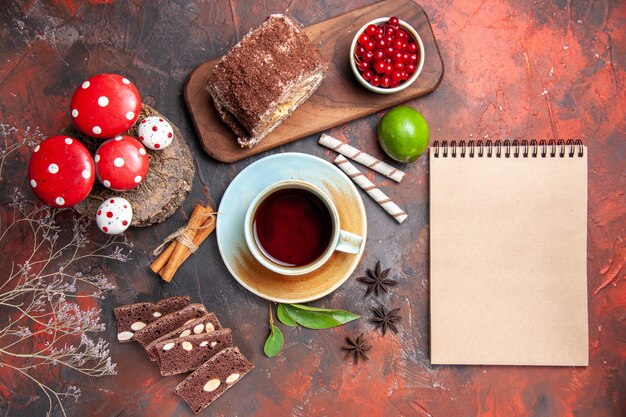 Vista superior de la taza de té con pastel y rollo de galletas sobre una superficie oscura