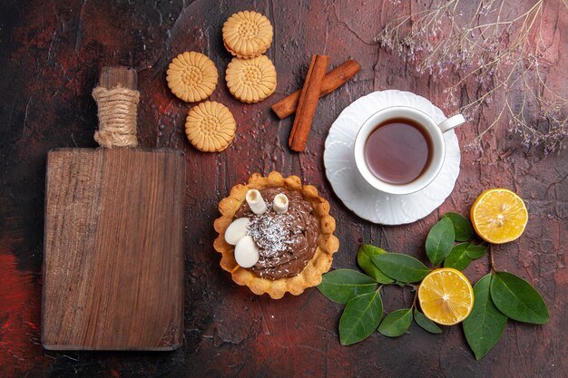 Vista superior de la taza de té con pastelito y galletas en la mesa oscura galleta de postre dulce