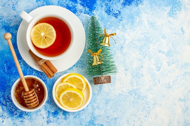 Vista superior taza de té pequeño árbol de Navidad rodajas de limón miel y palo de miel en un tazón en el espacio libre de la mesa azul