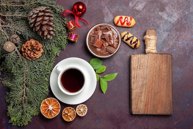 Vista superior de la taza de té con postre de chocolate y galletas en el espacio oscuro