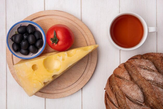 Foto gratuita vista superior taza de té con queso de aceitunas de tomate en un soporte y una hogaza de pan negro sobre un fondo blanco.