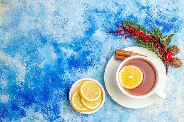 Vista superior taza de té rama de árbol de Navidad cortar limones en platillo en el lugar de copia de mesa azul